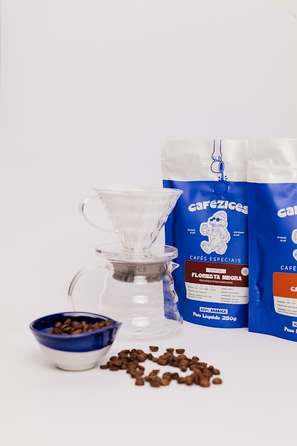 V60 com jarra e gr&atilde;os ao lado dos pacotes Floresta Negra e Caramelow